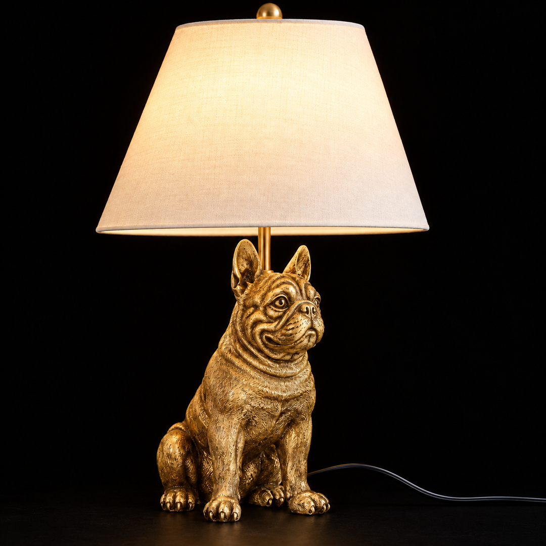 Gold French Bulldog table lamp with a white fabric shade, lit on a dark table